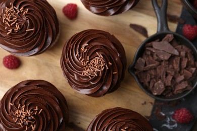 Photo of Tasty cupcakes with chocolate cream and raspberries on wooden table, flat lay