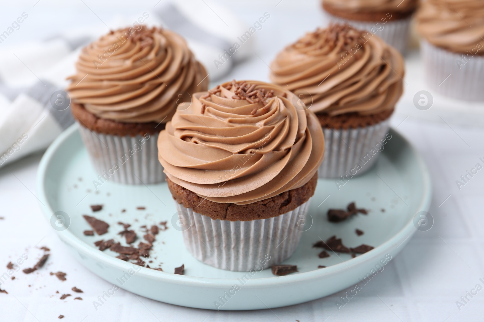 Photo of Tasty cupcakes with chocolate cream on white tiled table, closeup