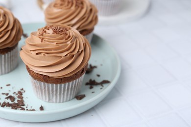 Photo of Tasty cupcakes with chocolate cream on white tiled table, closeup. Space for text