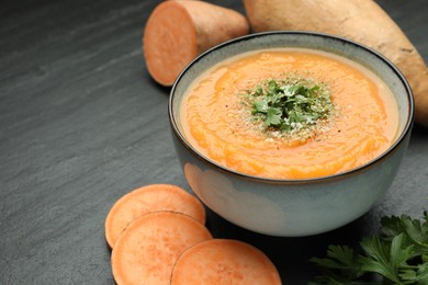 Photo of Delicious sweet potato soup with parmesan cheese in bowl and fresh ingredients on grey table, closeup