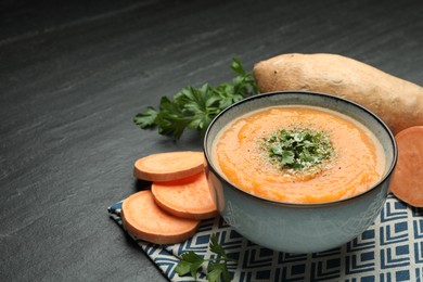 Photo of Delicious sweet potato soup with parmesan cheese in bowl and fresh ingredients on grey table, space for text