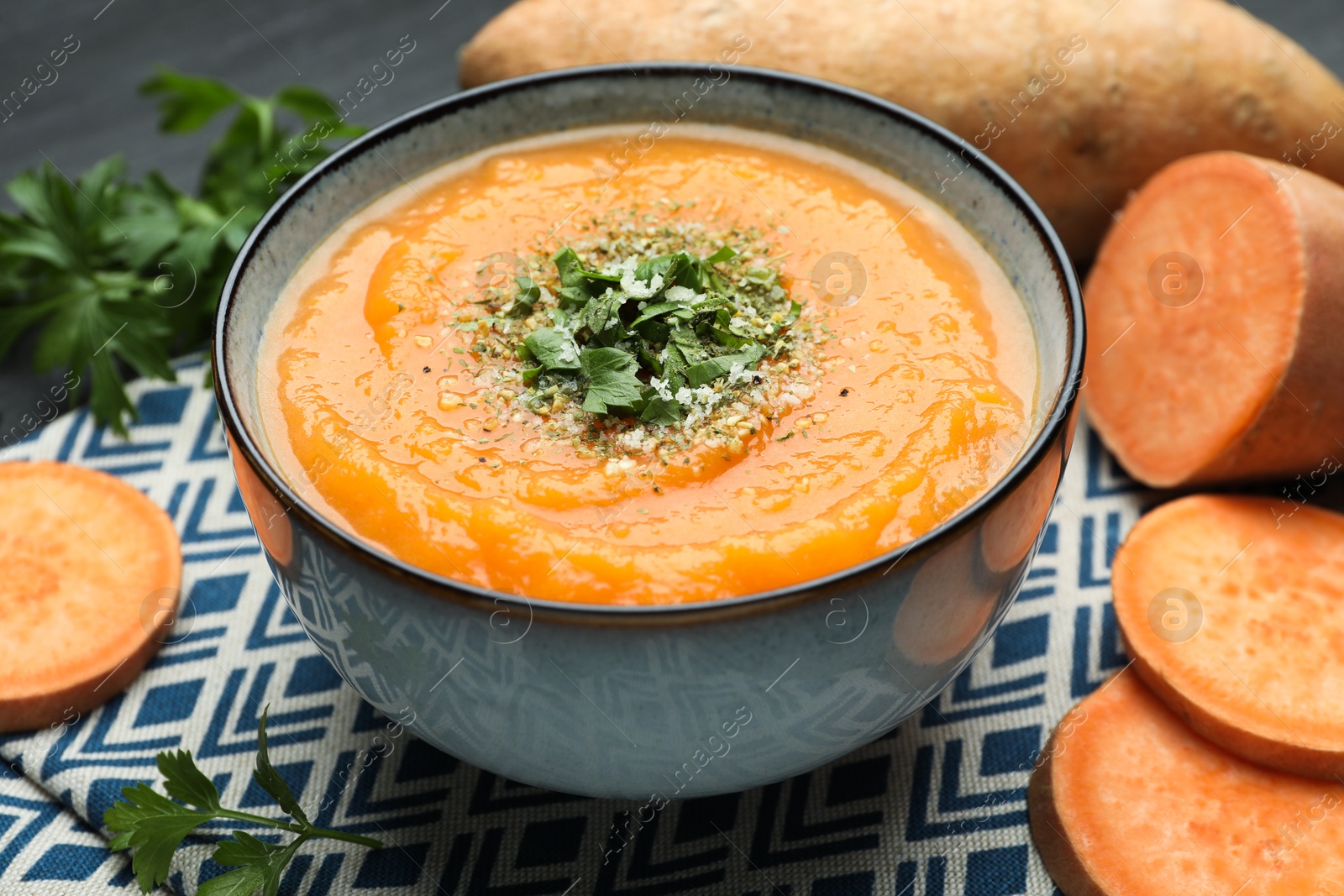 Photo of Delicious sweet potato soup with parmesan cheese in bowl and fresh ingredients on table, closeup