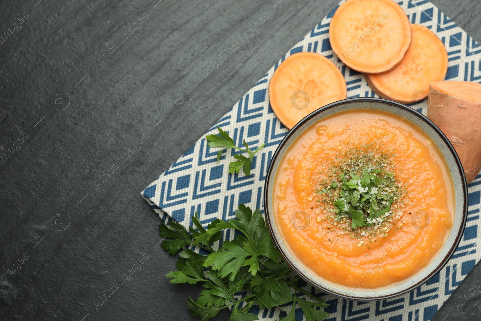 Photo of Delicious sweet potato soup with parmesan in bowl and fresh ingredients on grey textured table, flat lay. Space for text