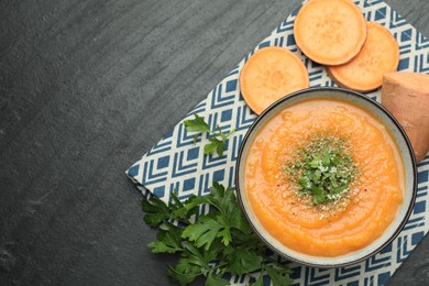 Photo of Delicious sweet potato soup with parmesan in bowl and fresh ingredients on grey textured table, flat lay. Space for text