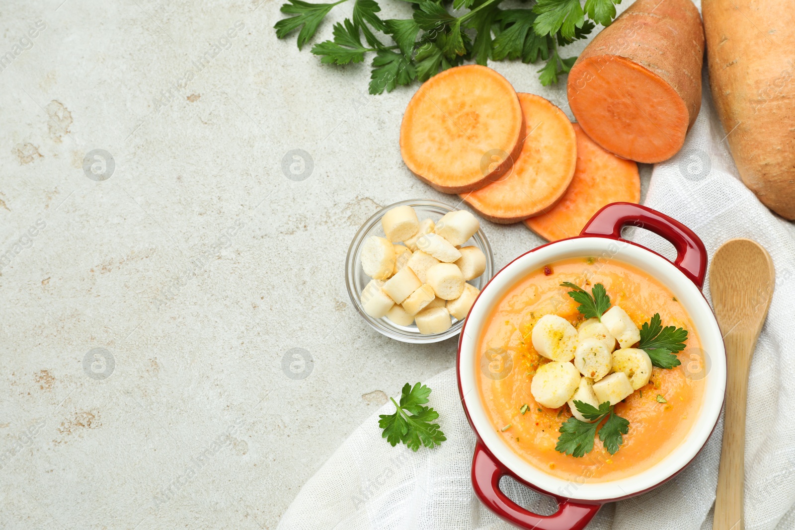 Photo of Delicious sweet potato soup with croutons and fresh ingredients on light textured table, flat lay. Space for text