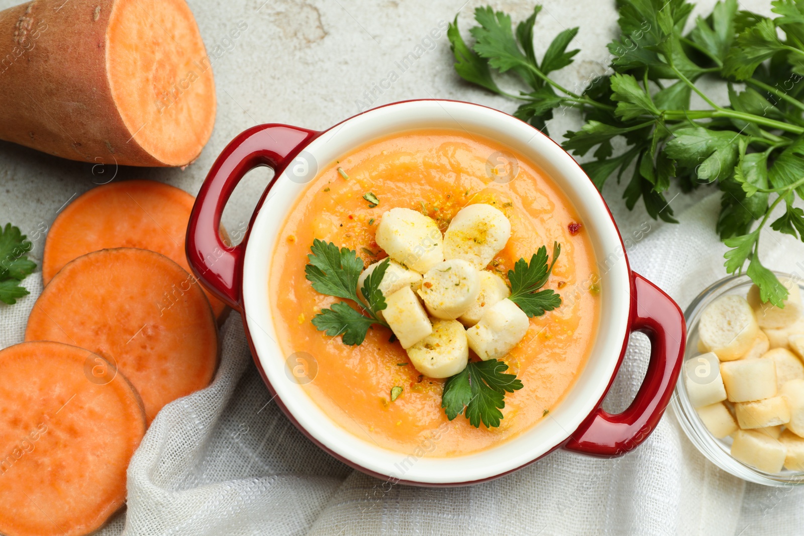 Photo of Delicious sweet potato soup with croutons and fresh ingredients on light textured table, flat lay