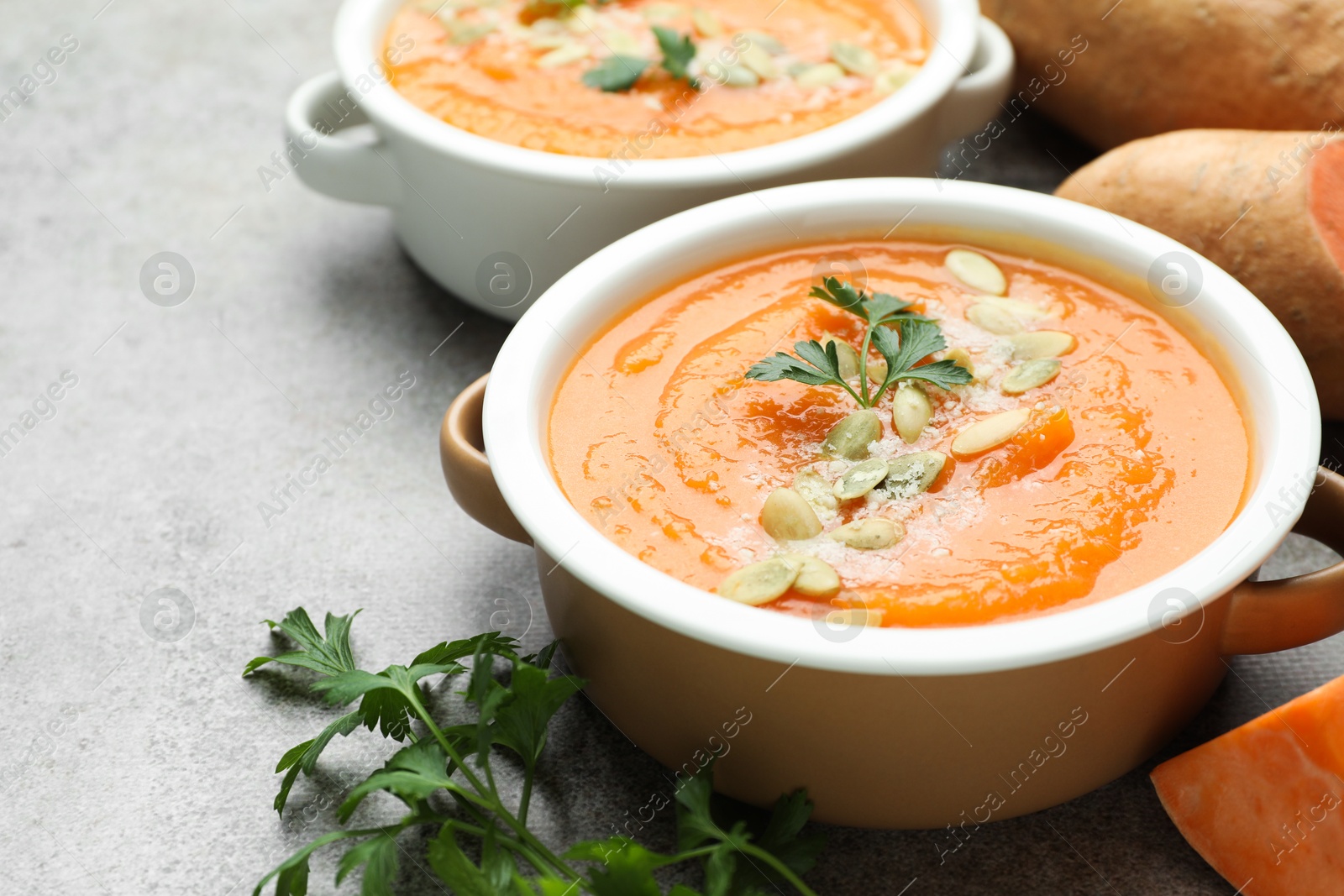 Photo of Delicious sweet potato soup with pumpkin seeds in bowls and fresh ingredients on grey table, closeup