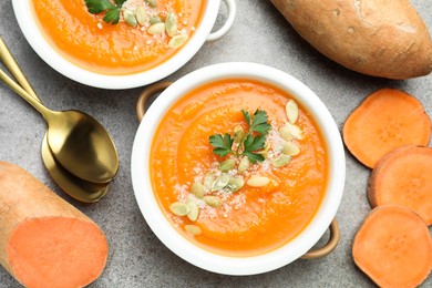 Photo of Delicious sweet potato soup with pumpkin seeds in bowls and fresh vegetables on grey textured table, flat lay