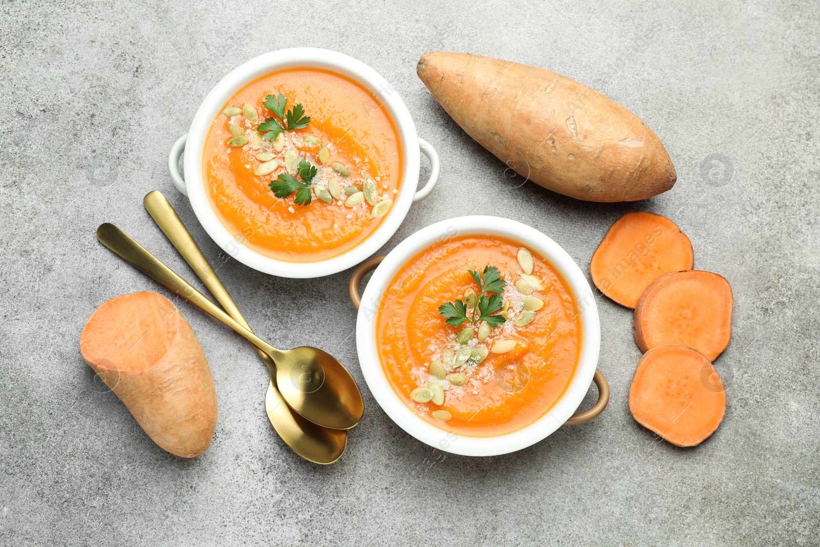 Photo of Delicious sweet potato soup with pumpkin seeds in bowls and fresh vegetables on grey textured table, flat lay