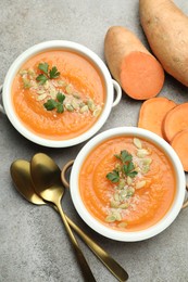 Photo of Delicious sweet potato soup with pumpkin seeds in bowls and fresh vegetables on grey textured table, flat lay