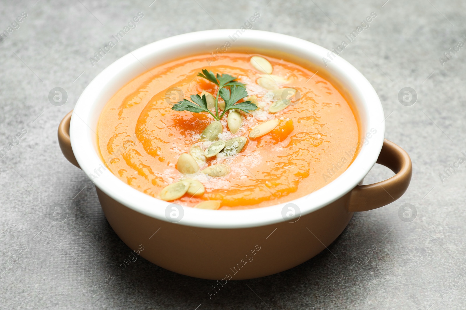 Photo of Delicious sweet potato soup with pumpkin seeds and parsley in bowl on grey textured table, closeup