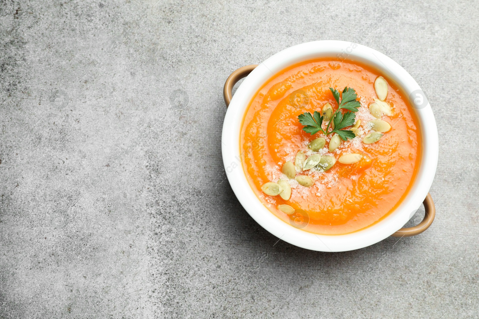 Photo of Delicious sweet potato soup with pumpkin seeds and parsley in bowl on grey textured table, top view. Space for text