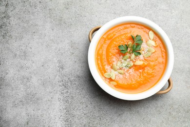 Photo of Delicious sweet potato soup with pumpkin seeds and parsley in bowl on grey textured table, top view. Space for text