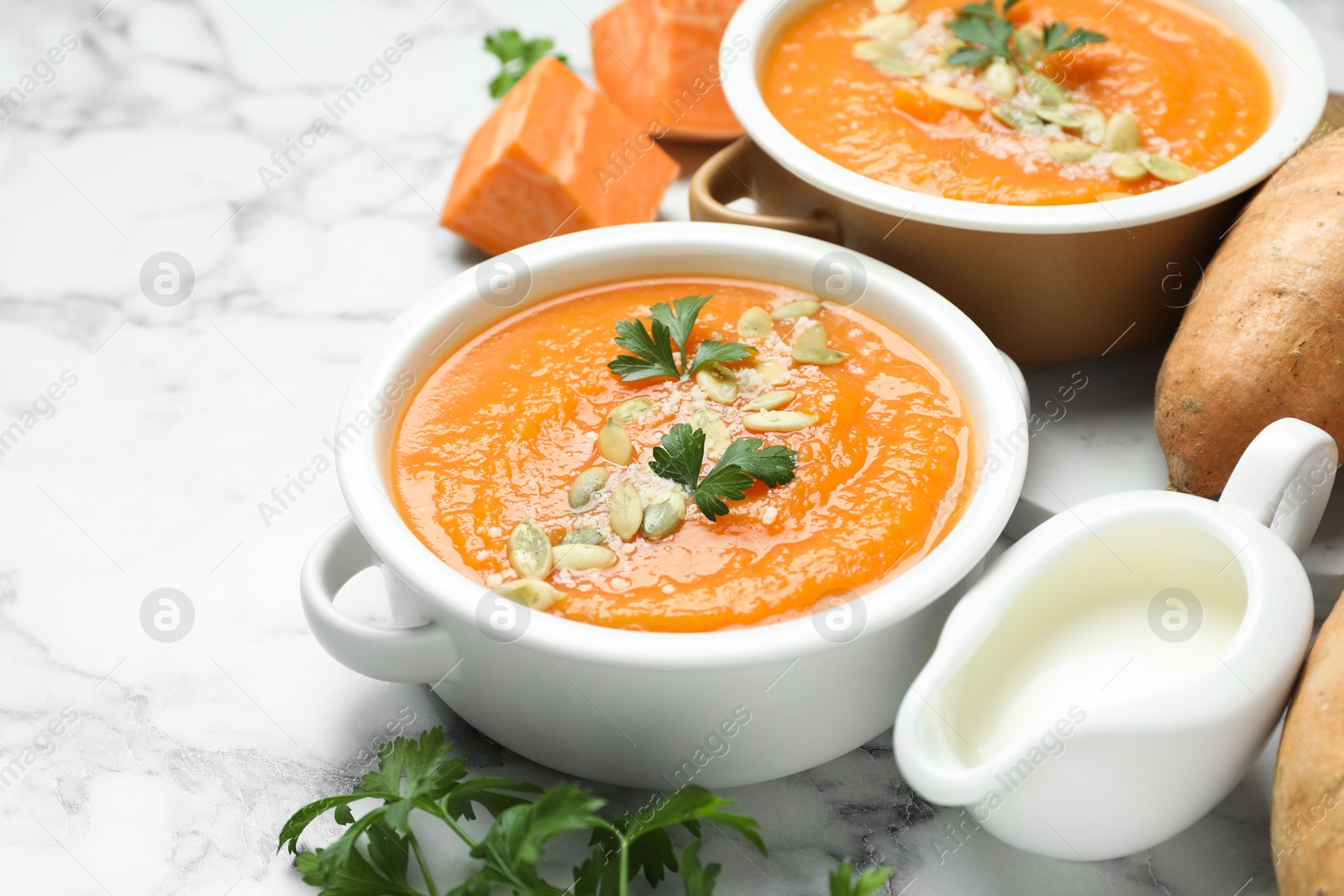 Delicious sweet potato soup with pumpkin seeds and parsley in bowls served on white marble table, closeup Photo of Delicious sweet potato soup with pumpkin seeds and parsley in bowls served on white marble table, closeup
