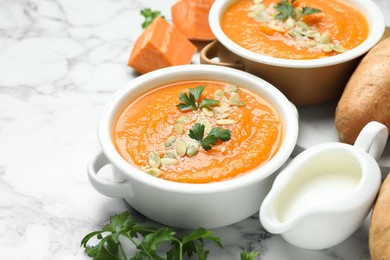 Photo of Delicious sweet potato soup with pumpkin seeds and parsley in bowls served on white marble table, closeup