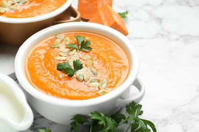 Photo of Delicious sweet potato soup with pumpkin seeds and parsley in bowls served on white marble table, closeup