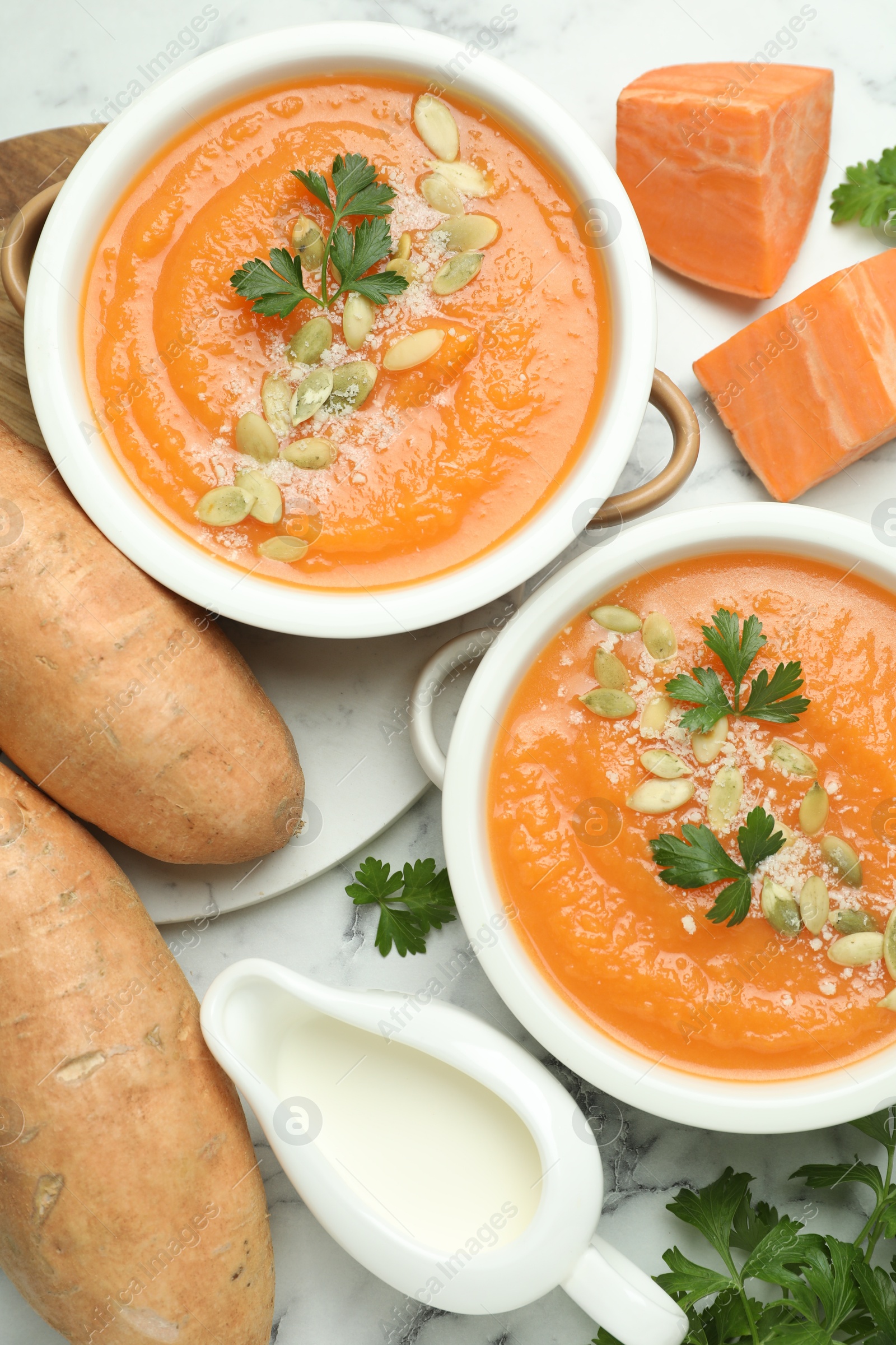 Photo of Delicious sweet potato soup with pumpkin seeds in bowls served on white marble table, flat lay