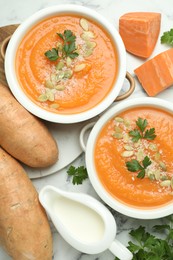 Photo of Delicious sweet potato soup with pumpkin seeds in bowls served on white marble table, flat lay