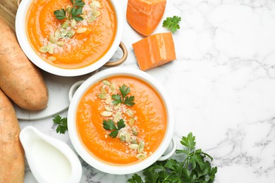 Photo of Delicious sweet potato soup with pumpkin seeds in bowls served on white marble table, flat lay. Space for text