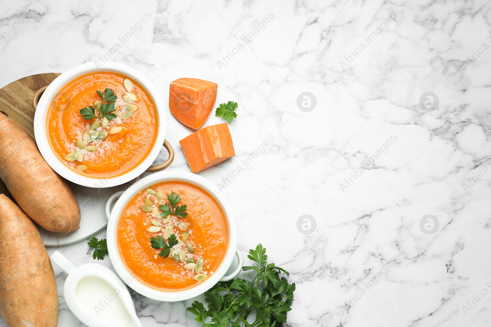 Photo of Delicious sweet potato soup with pumpkin seeds in bowls served on white marble table, flat lay. Space for text