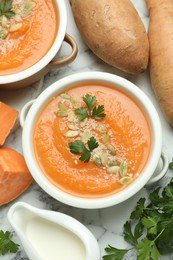 Photo of Delicious sweet potato soup with pumpkin seeds in bowls served on white marble table, flat lay