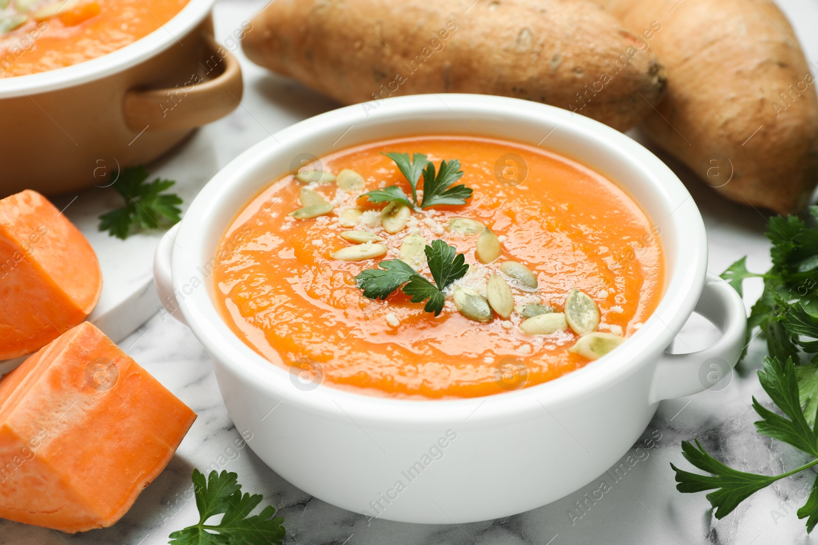 Photo of Delicious sweet potato soup with fresh ingredients on white marble table, closeup