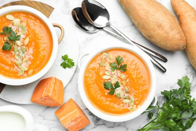 Photo of Delicious sweet potato soup with pumpkin seeds in bowls served on white marble table, flat lay