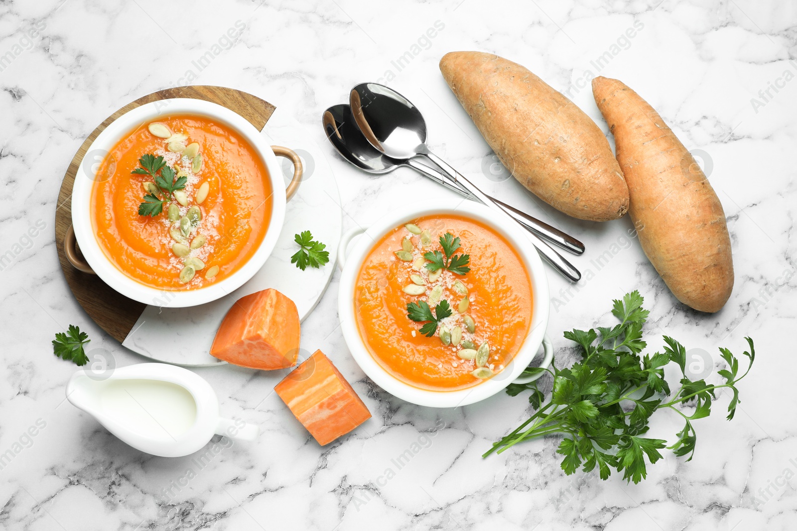Delicious sweet potato soup with pumpkin seeds in bowls served on white marble table, flat lay Photo of Delicious sweet potato soup with pumpkin seeds in bowls served on white marble table, flat lay