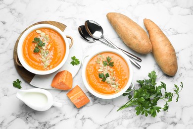 Photo of Delicious sweet potato soup with pumpkin seeds in bowls served on white marble table, flat lay