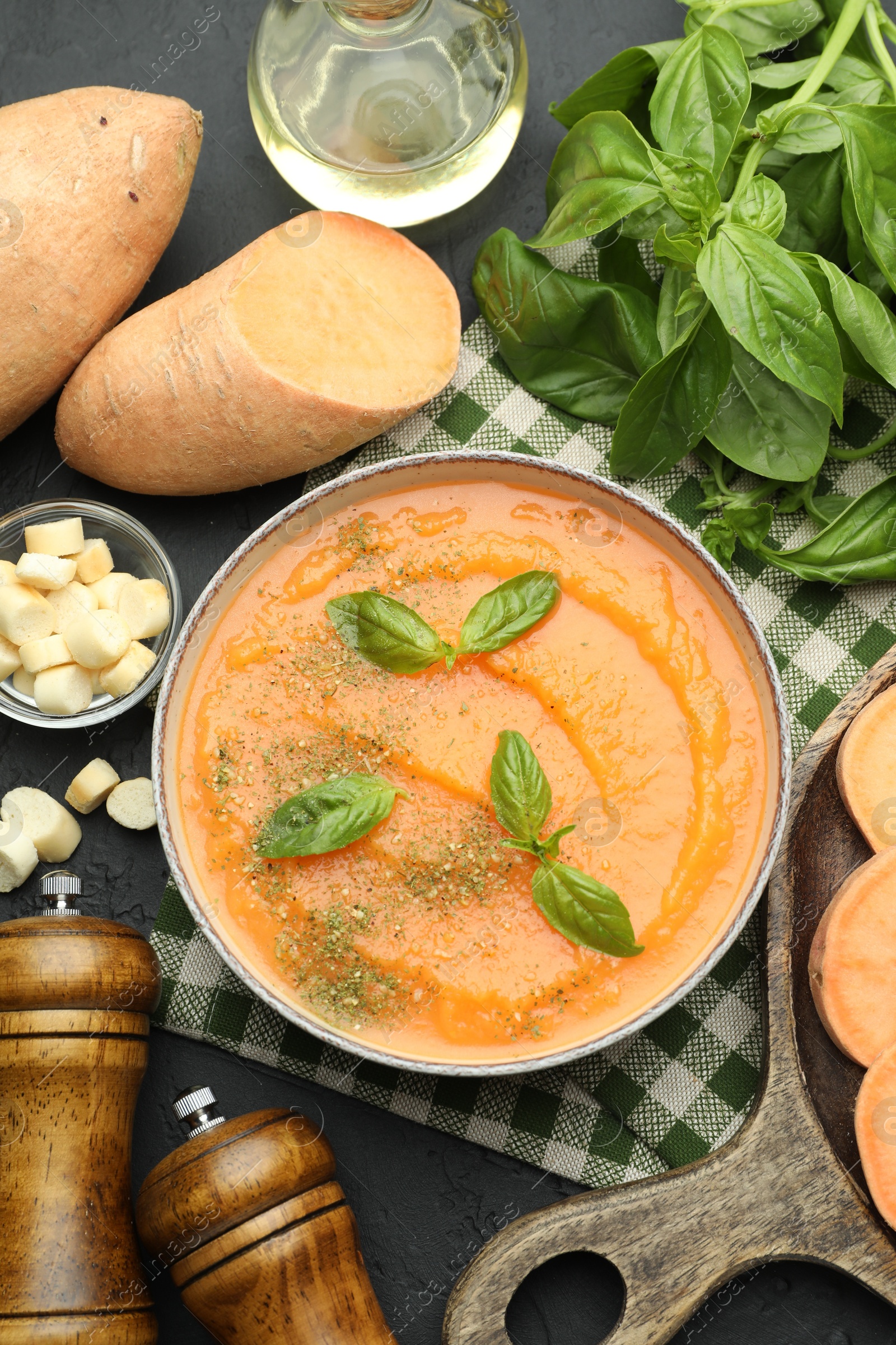 Photo of Delicious sweet potato soup in bowl with croutons and fresh ingredients on grey textured table, flat lay