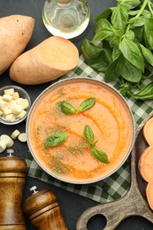 Photo of Delicious sweet potato soup in bowl with croutons and fresh ingredients on grey textured table, flat lay