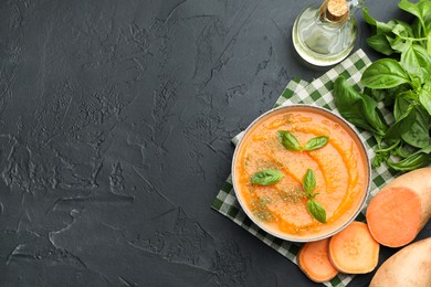 Photo of Delicious sweet potato soup in bowl with fresh ingredients on grey textured table, flat lay. Space for text