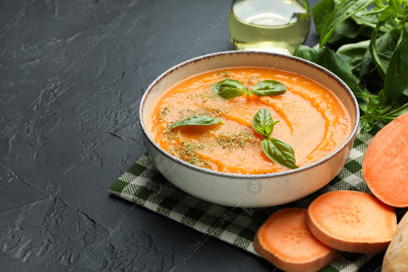 Photo of Delicious sweet potato soup in bowl and fresh ingredients on grey textured table