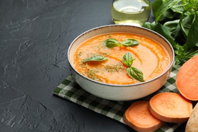 Photo of Delicious sweet potato soup in bowl and fresh ingredients on grey textured table