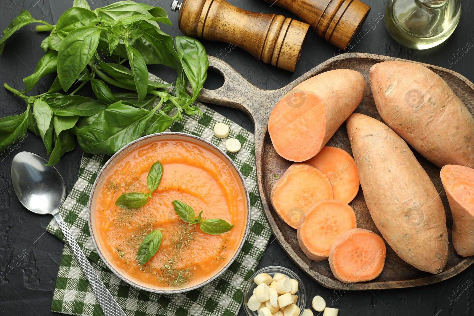 Photo of Delicious sweet potato soup in bowl with croutons and fresh ingredients on grey textured table, flat lay