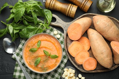 Photo of Delicious sweet potato soup in bowl with croutons and fresh ingredients on grey textured table, flat lay