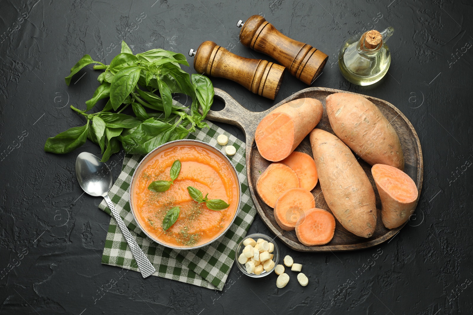 Photo of Delicious sweet potato soup in bowl with croutons and fresh ingredients on grey textured table, flat lay