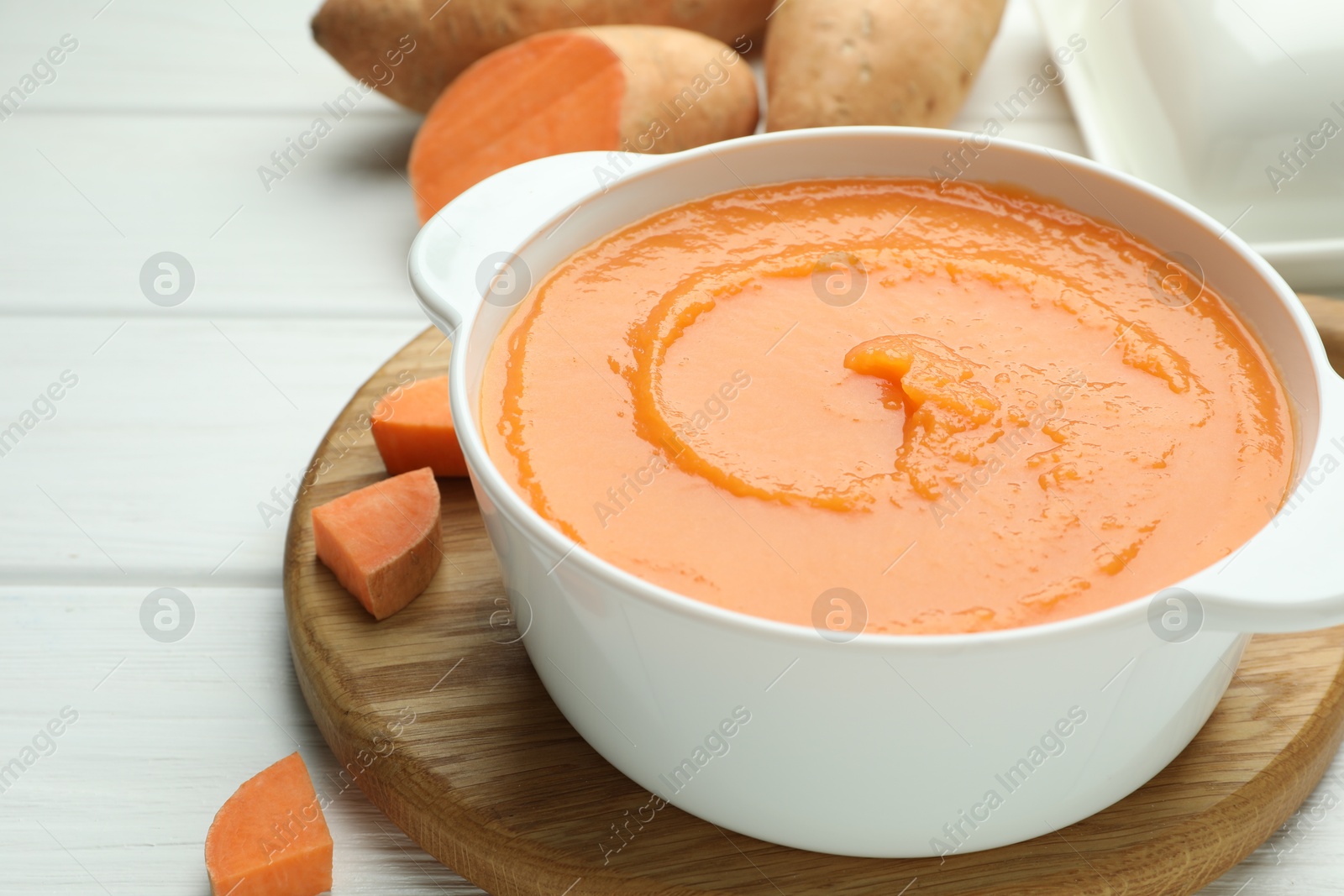 Photo of Delicious sweet potato soup with fresh vegetable on white wooden table, closeup