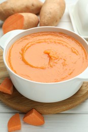 Photo of Delicious sweet potato soup with fresh vegetable on white wooden table, closeup