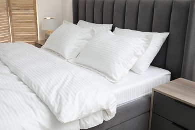 Comfortable bed with clean linens and pillows indoors