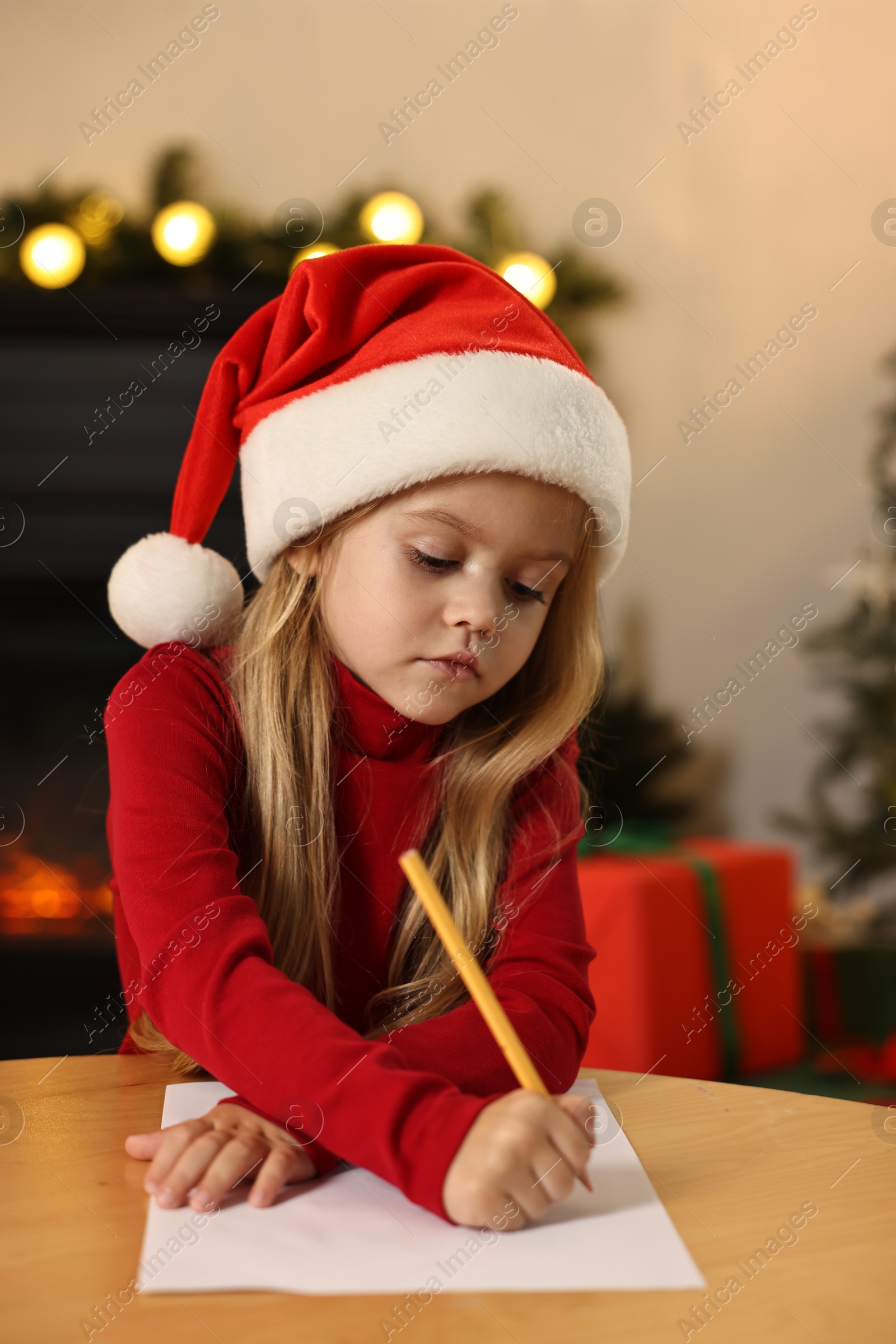 Photo of Little girl writing letter to Santa Claus at table indoors. Christmas celebration