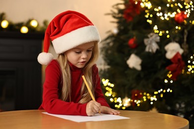 Little girl writing letter to Santa Claus at table indoors. Christmas celebration