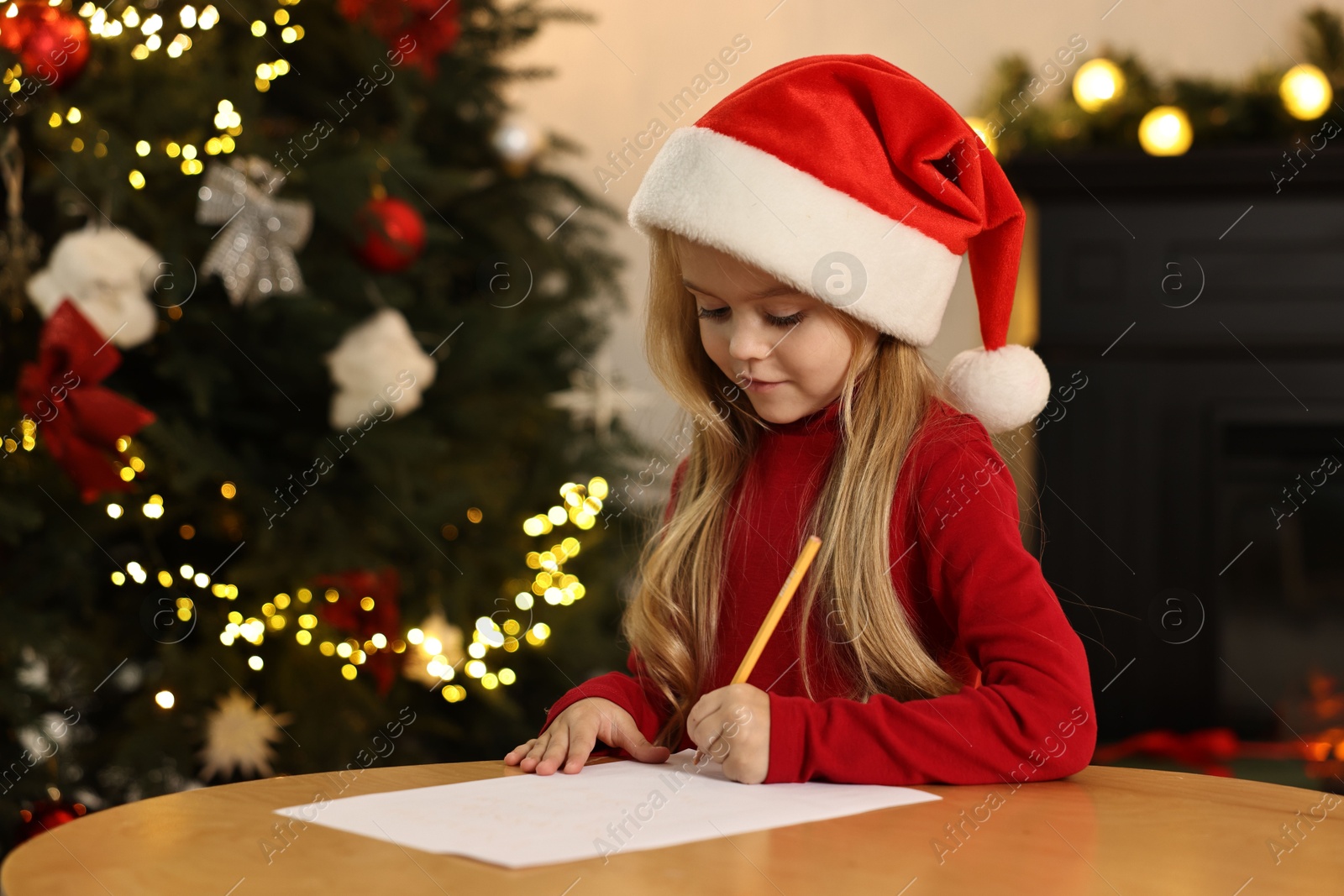 Photo of Little girl writing letter to Santa Claus at table indoors. Christmas celebration