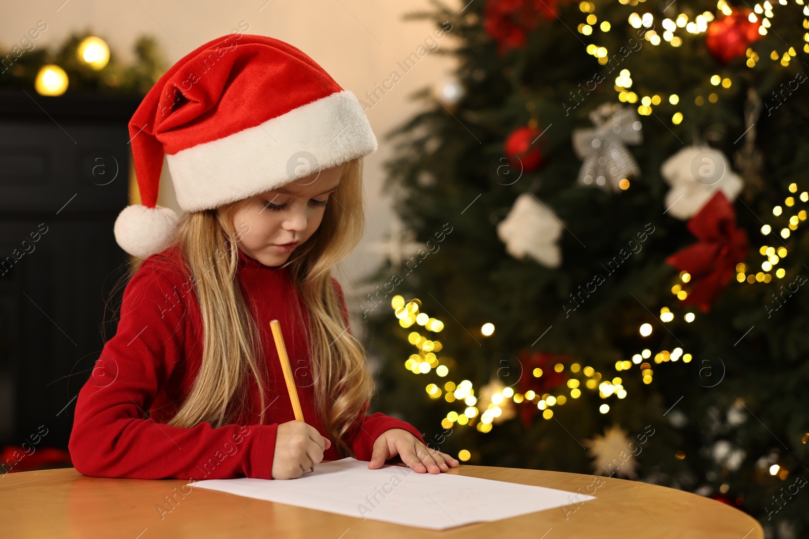 Photo of Little girl writing letter to Santa Claus at table indoors. Christmas celebration