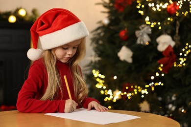 Photo of Little girl writing letter to Santa Claus at table indoors. Christmas celebration