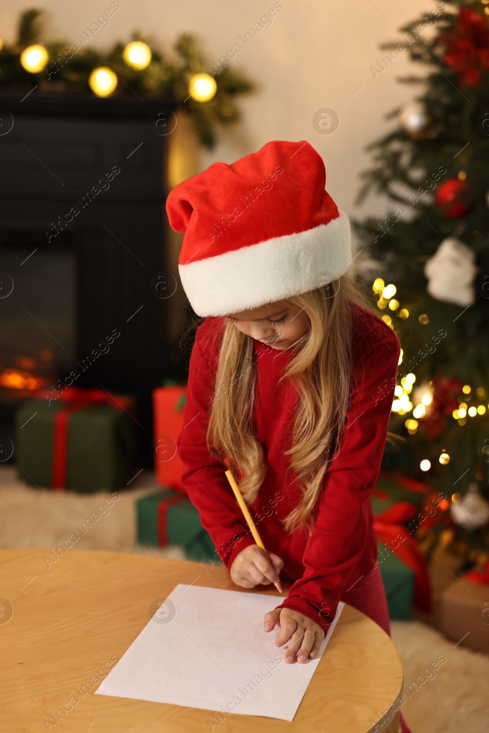 Photo of Little girl writing letter to Santa Claus at table indoors. Christmas celebration