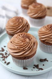 Photo of Tasty cupcakes with chocolate cream on white tiled table, closeup