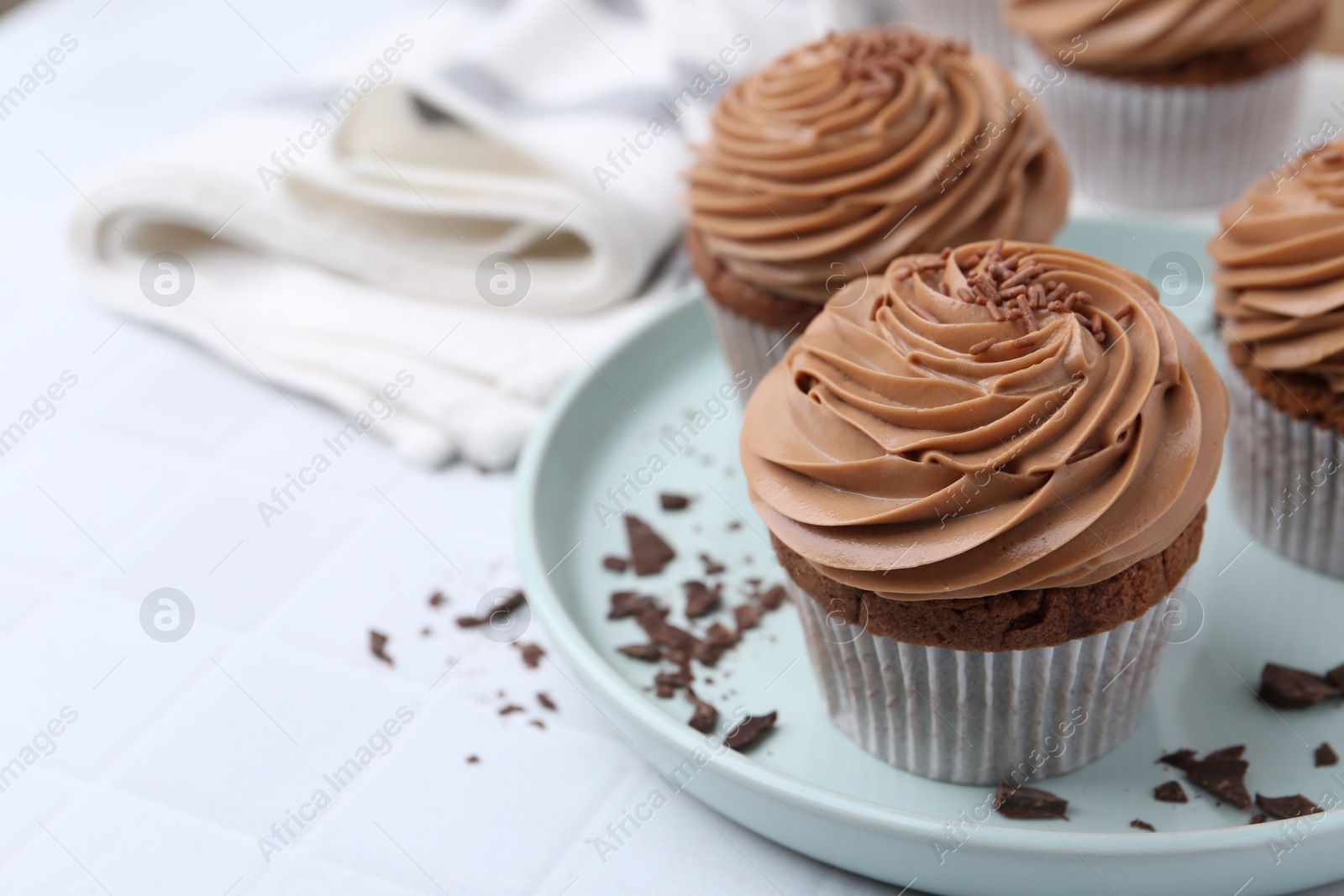 Photo of Tasty cupcakes with chocolate cream on white tiled table, closeup. Space for text