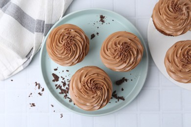 Photo of Tasty cupcakes with chocolate cream on white tiled table, flat lay