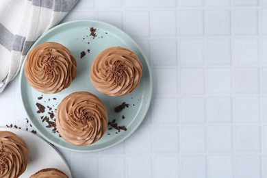 Photo of Tasty cupcakes with chocolate cream on white tiled table, flat lay. Space for text